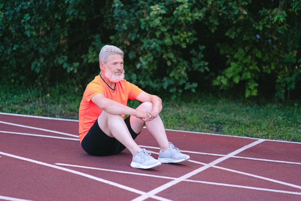 sporty senior man sitting on stadium track